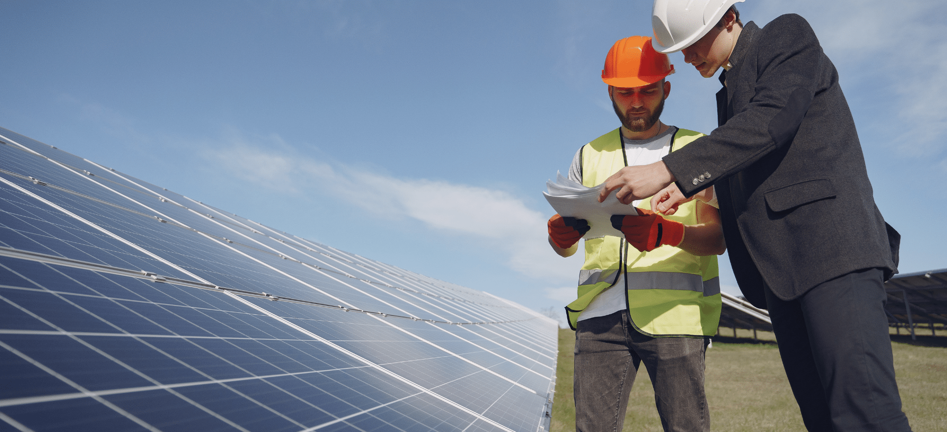Two solar industry professionals in safety gear reviewing documents beside a large solar panel array under a clear sky, symbolizing proactive planning for solar waste management.