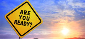 A bold yellow road sign with the words “ARE YOU READY?” set against a colorful sunrise sky, representing the urgent need to prepare for the upcoming surge in solar waste.