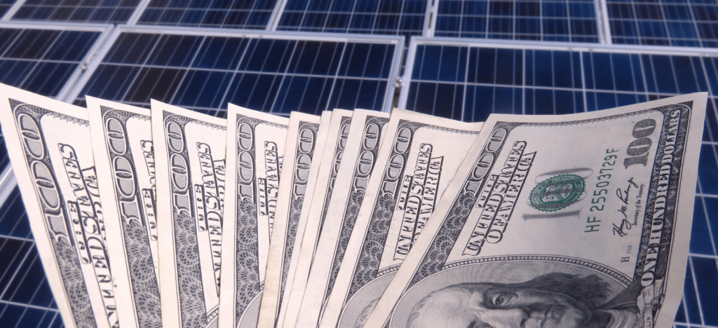 A fan of hundred-dollar bills in front of solar panels, symbolizing the financial value recovered from used photovoltaic equipment.