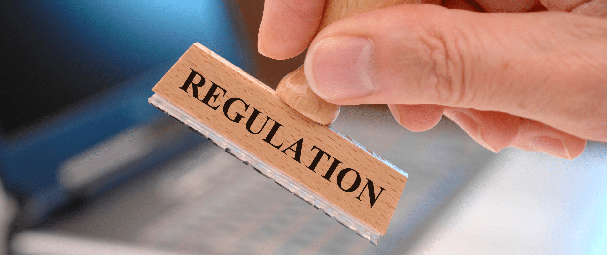 A close-up of a hand pressing a wooden stamp labeled “REGULATION” against a blurred office background, representing the legal and regulatory aspects of commercial solar panel disposal in the United States.